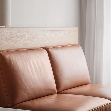 Copenhagen Admiral Hotel Esterno foto The photo shows a modern, minimalist seating area featuring a tan leather sofa with two cushions. The back of the sofa is against a light wooden panel, which adds a natural element to the decor. There are sheer curtains in the background, allowing so