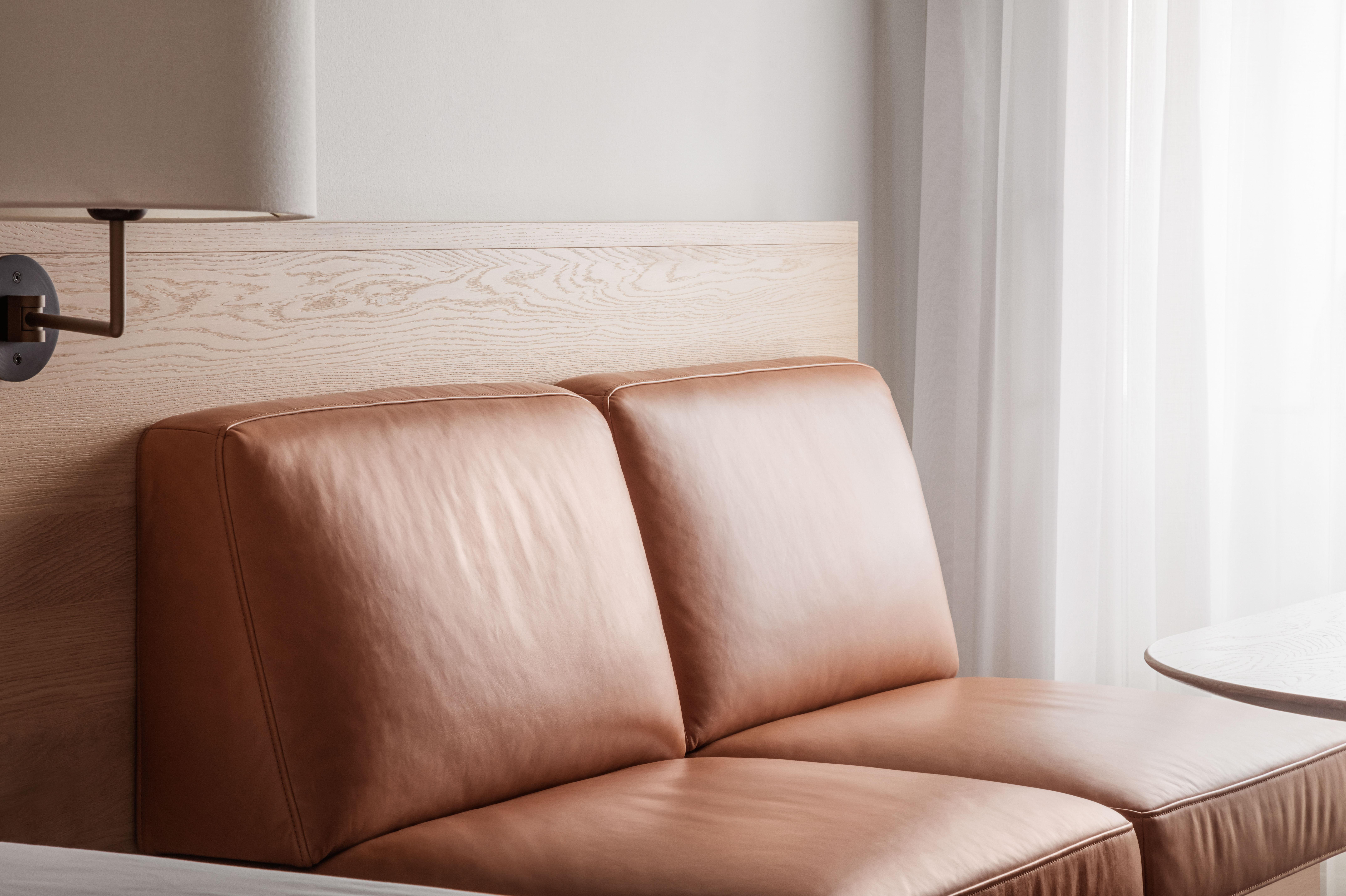 Copenhagen Admiral Hotel Esterno foto The photo shows a modern, minimalist seating area featuring a tan leather sofa with two cushions. The back of the sofa is against a light wooden panel, which adds a natural element to the decor. There are sheer curtains in the background, allowing so