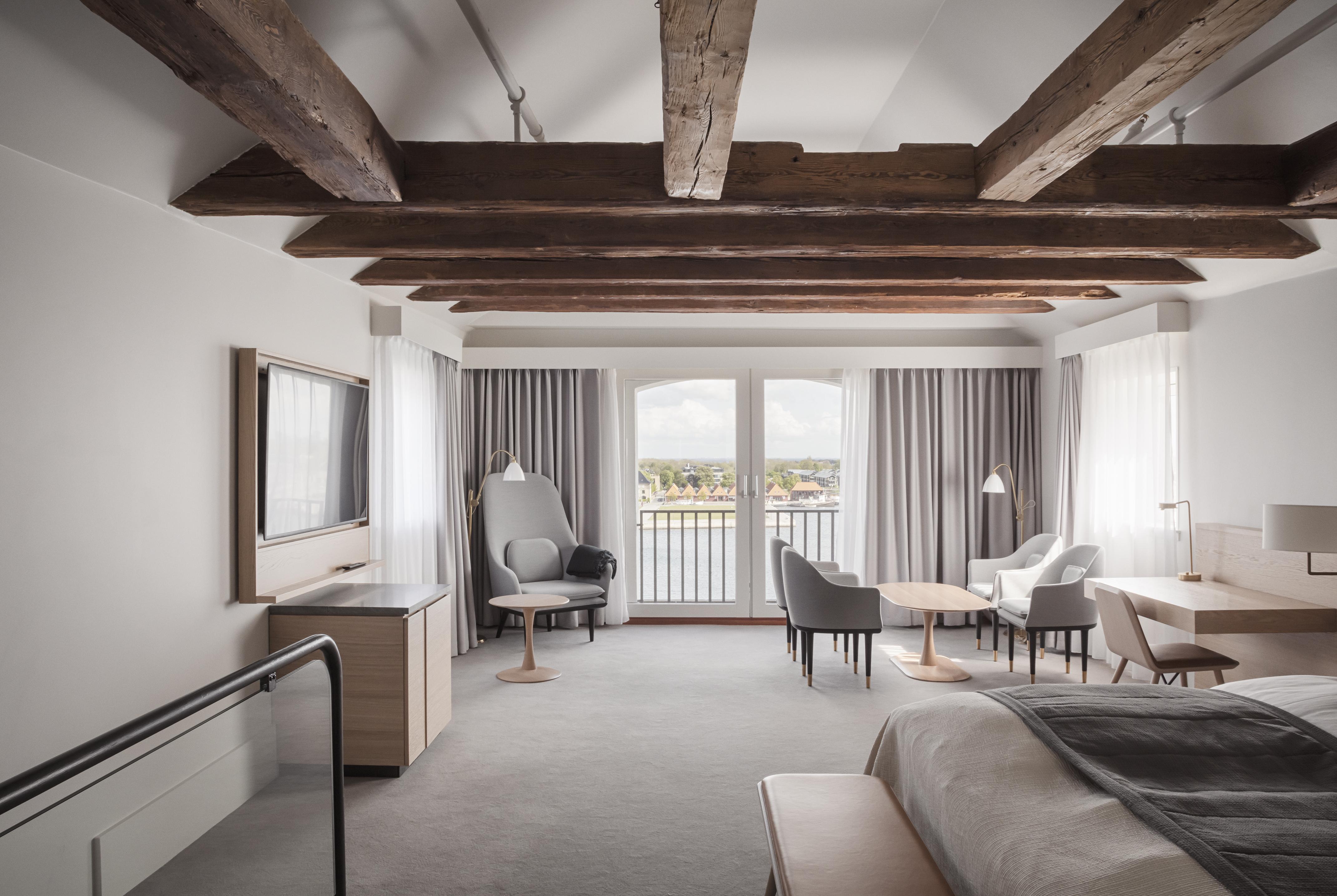Copenhagen Admiral Hotel Esterno foto The photo shows a modern hotel room featuring a spacious and stylish design. The room has exposed wooden beams in the ceiling, adding a rustic touch. There is a large bed with neutral-colored bedding, and two windows dressed with soft curtains, allow