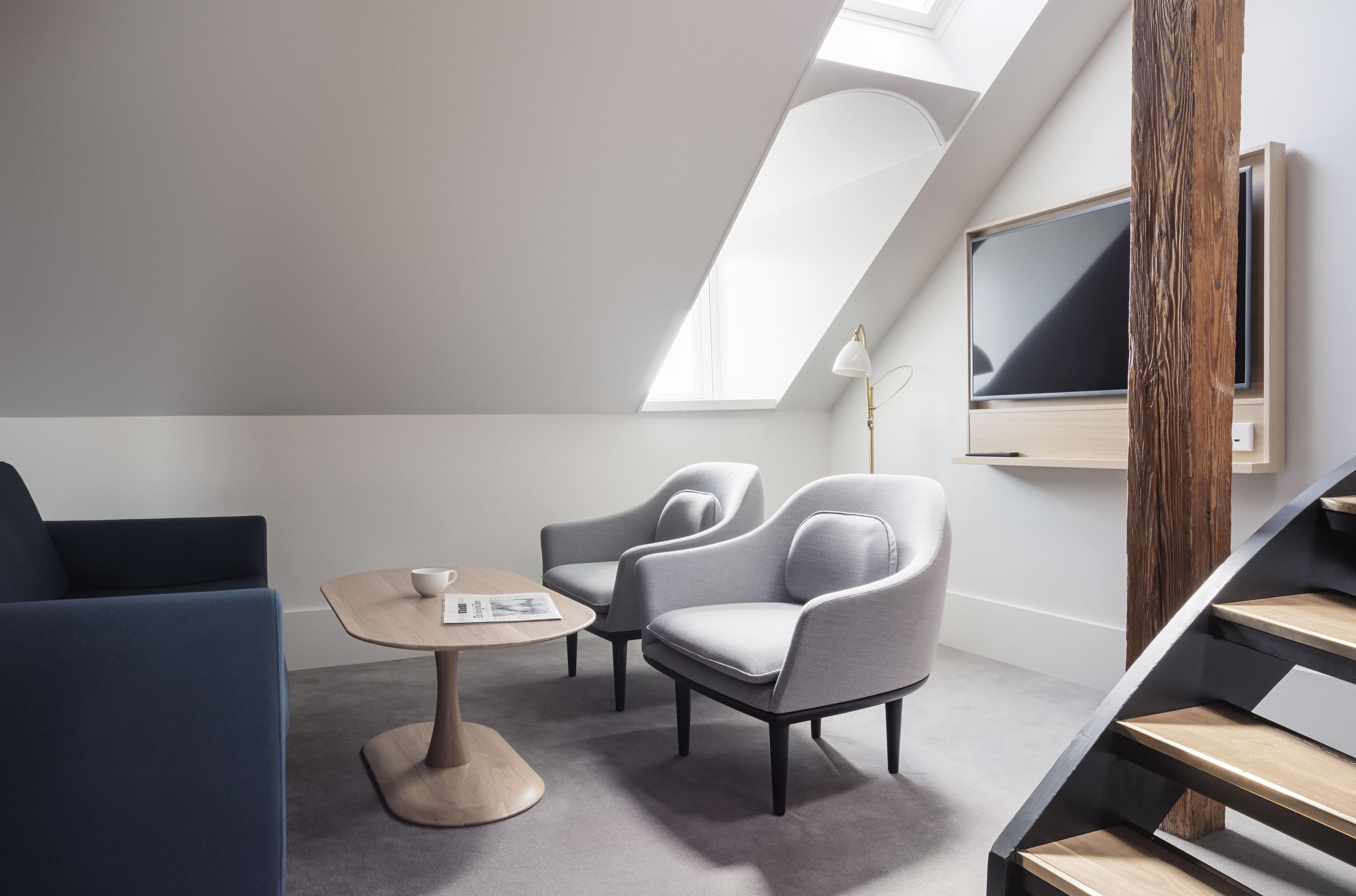 Copenhagen Admiral Hotel Esterno foto The photo shows an interior space designed with a modern aesthetic. It features two light gray armchairs positioned around a round wooden coffee table. A flat-screen television is mounted on the wall to the right. There is a tall, slender lamp beside