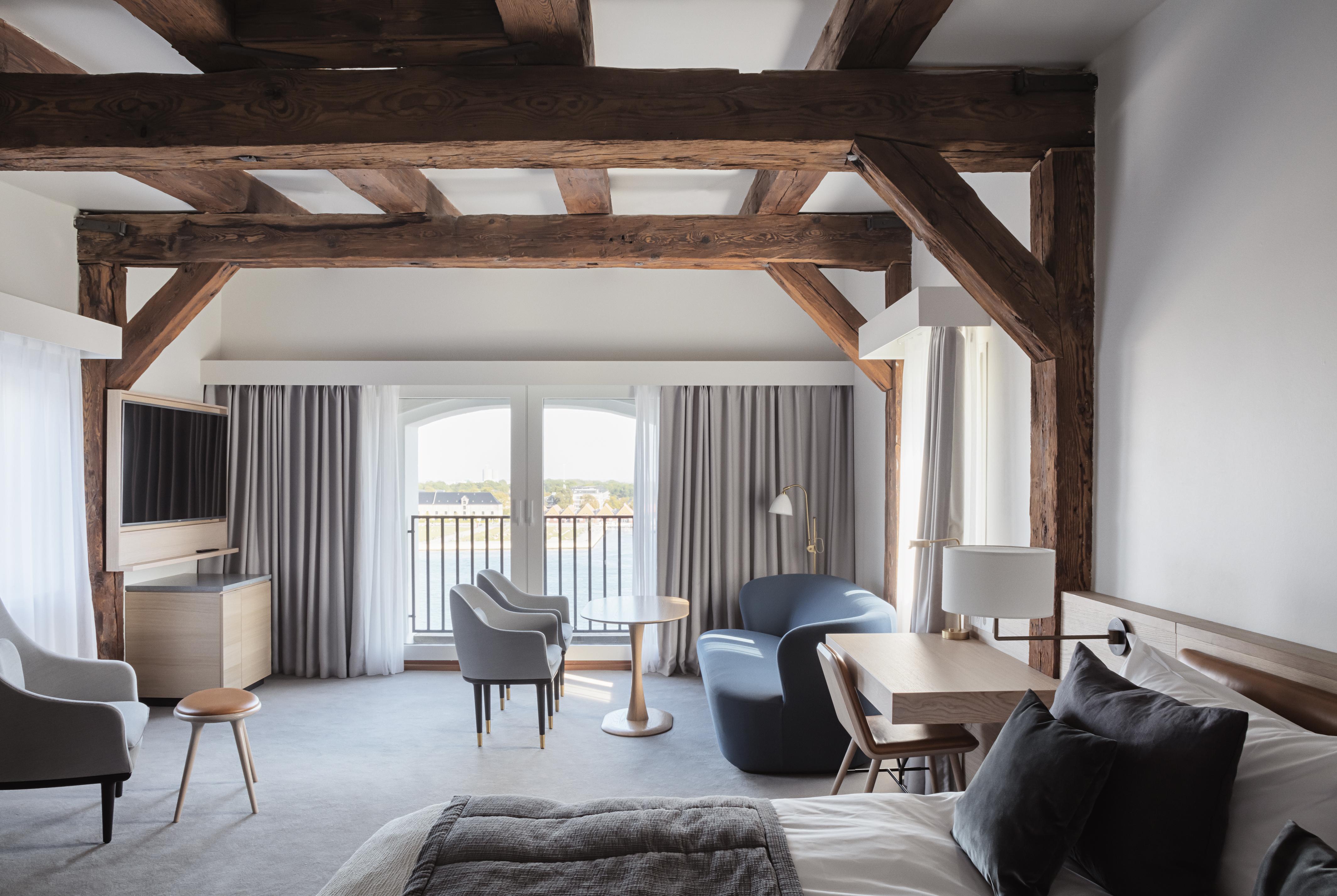 Copenhagen Admiral Hotel Esterno foto The photo shows a stylish hotel room featuring a modern and cozy design. The room has wooden beams in the ceiling, which adds a rustic touch. There's a comfortable bed with soft linens and a grey throw blanket. A sitting area includes two chairs (one