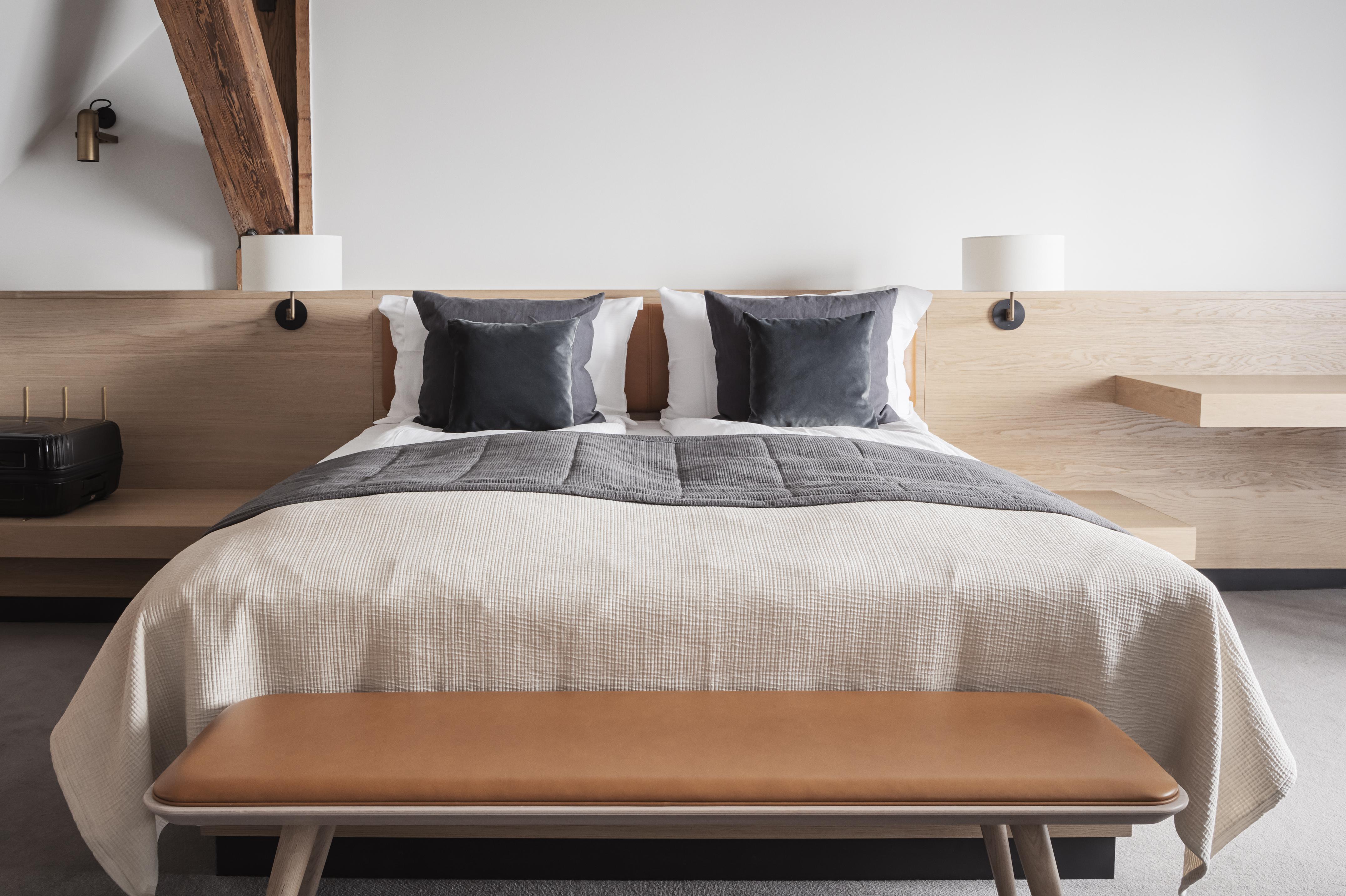 Copenhagen Admiral Hotel Esterno foto The photo shows a modern bedroom featuring a neatly made bed with light-colored bedding. The bed has two decorative pillows in darker shades placed at the headboard. There is a simple wooden bench at the foot of the bed. The walls have wooden beam ac