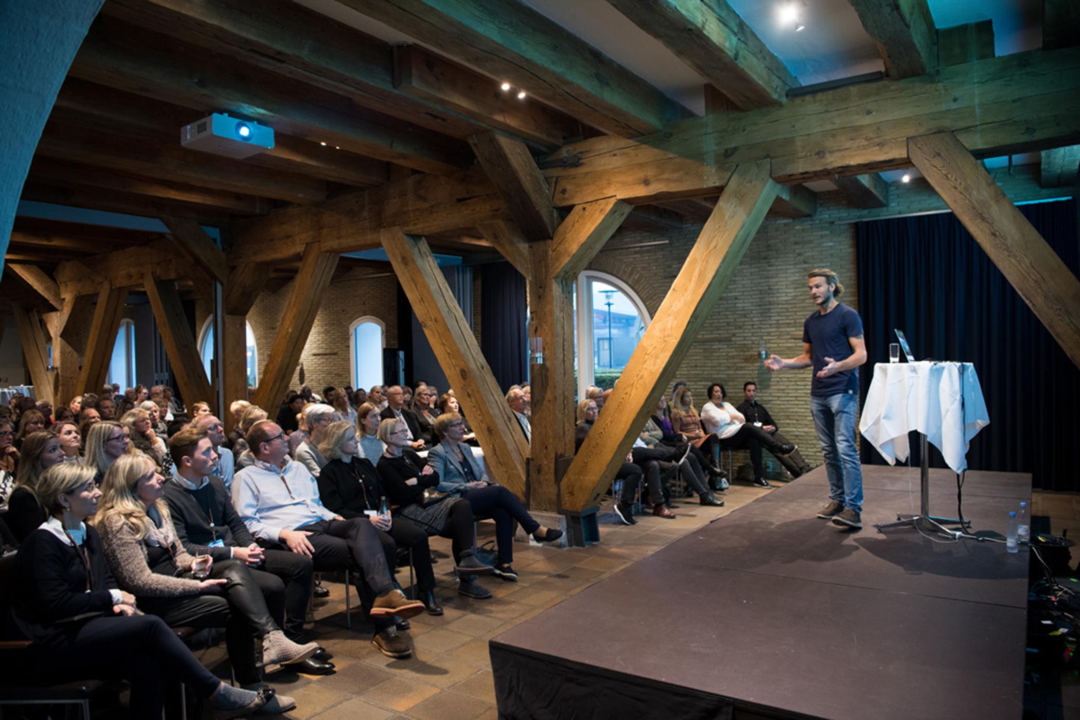 Copenhagen Admiral Hotel Esterno foto The photo shows a speaker standing on a stage in front of a large audience. The venue features exposed wooden beams and a modern interior design. The audience, consisting of many seated individuals, appears engaged as they watch the speaker, who is l