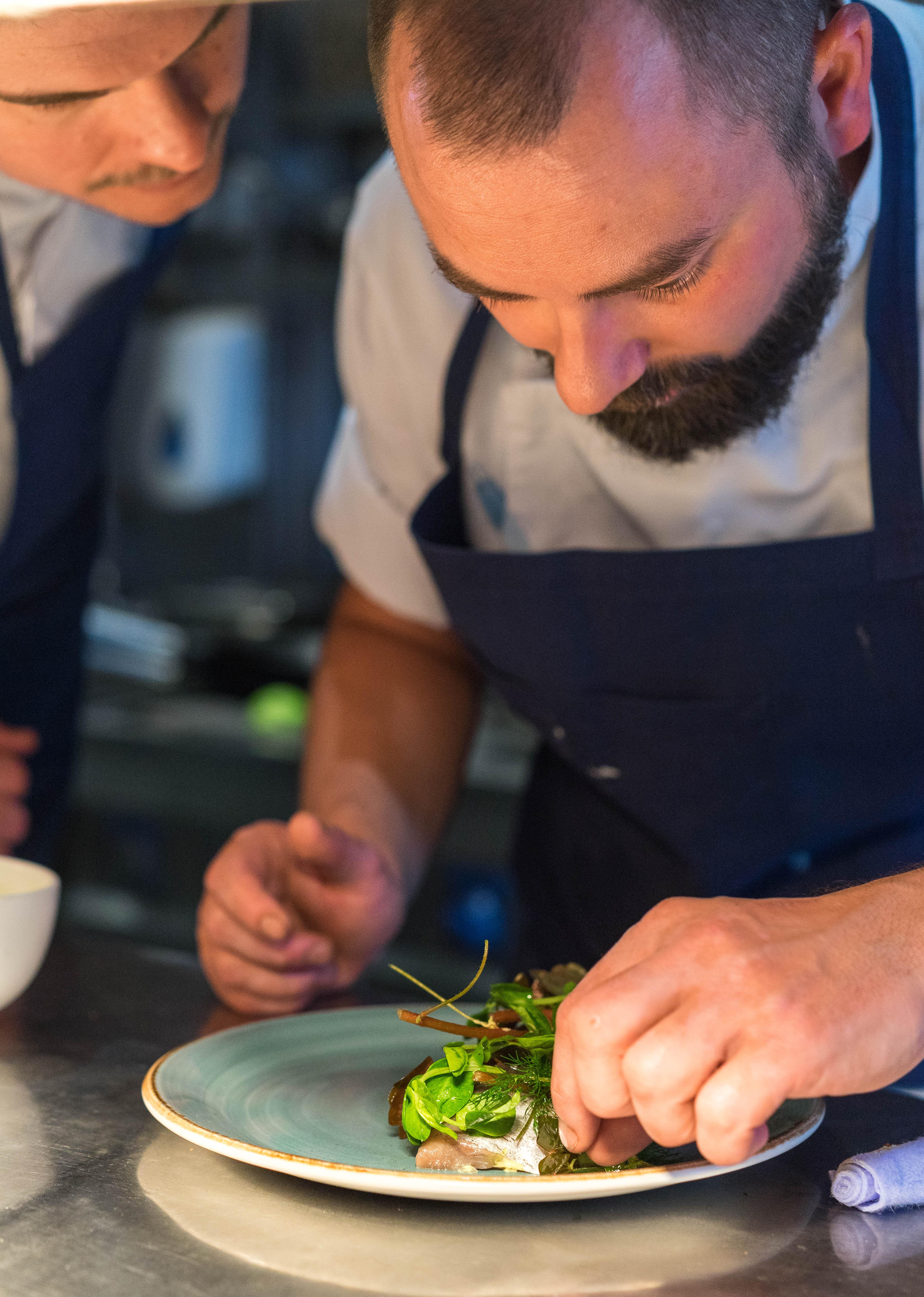 Copenhagen Admiral Hotel Esterno foto The photo shows a close-up of a chef focused on plating a dish. He has a beard and is wearing a white chef's jacket with a dark apron. His attention is directed towards the food, which appears to be carefully arranged on a plate. The background sugge