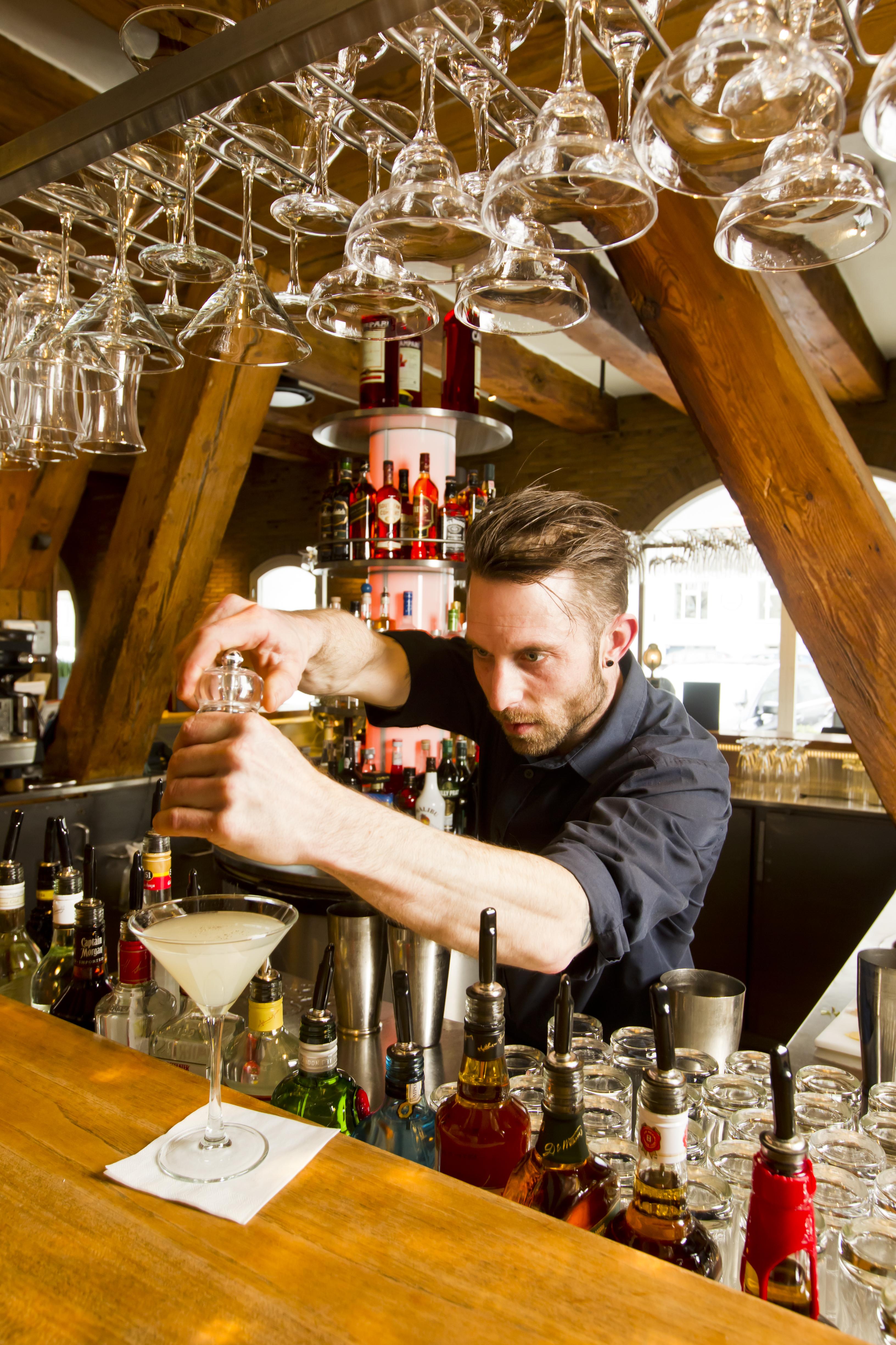 Copenhagen Admiral Hotel Esterno foto The photo depicts a bartender mixing a cocktail at a bar. He is focused on his task, using a shaker to prepare a drink. The bar is well-stocked with various bottles of liquor and mixers visible in the background. The setting features wooden beams and