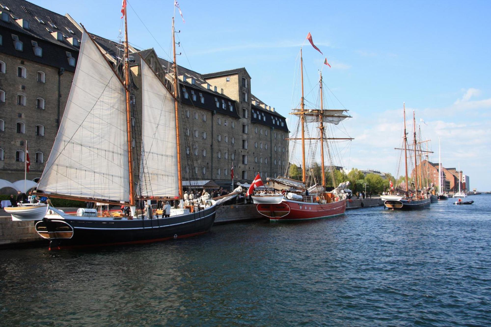 Copenhagen Admiral Hotel Esterno foto The photo captures a scenic harbor view featuring several traditional sailboats docked along a canal. The boats include a larger ship with billowing white sails and notable rigging, alongside smaller vessels. In the background, there are historic bui