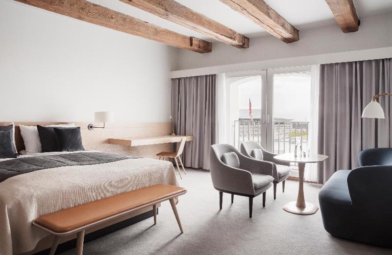 Copenhagen Admiral Hotel Camera foto The photo shows a spacious hotel room featuring modern decor and a cozy atmosphere. A large bed with a soft blanket is positioned against one wall, complemented by a bedside lamp. There is a small desk and chair nearby, ideal for working or studying.