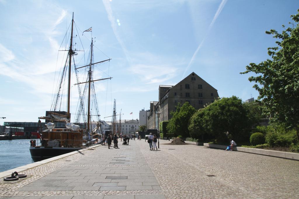 Copenhagen Admiral Hotel Esterno foto The photo depicts a scenic waterfront area with a cobblestone walkway beside a harbor. On one side, there are several tall ships with masts and sails docked, indicating a maritime setting. The buildings in the background appear to be modern or renova