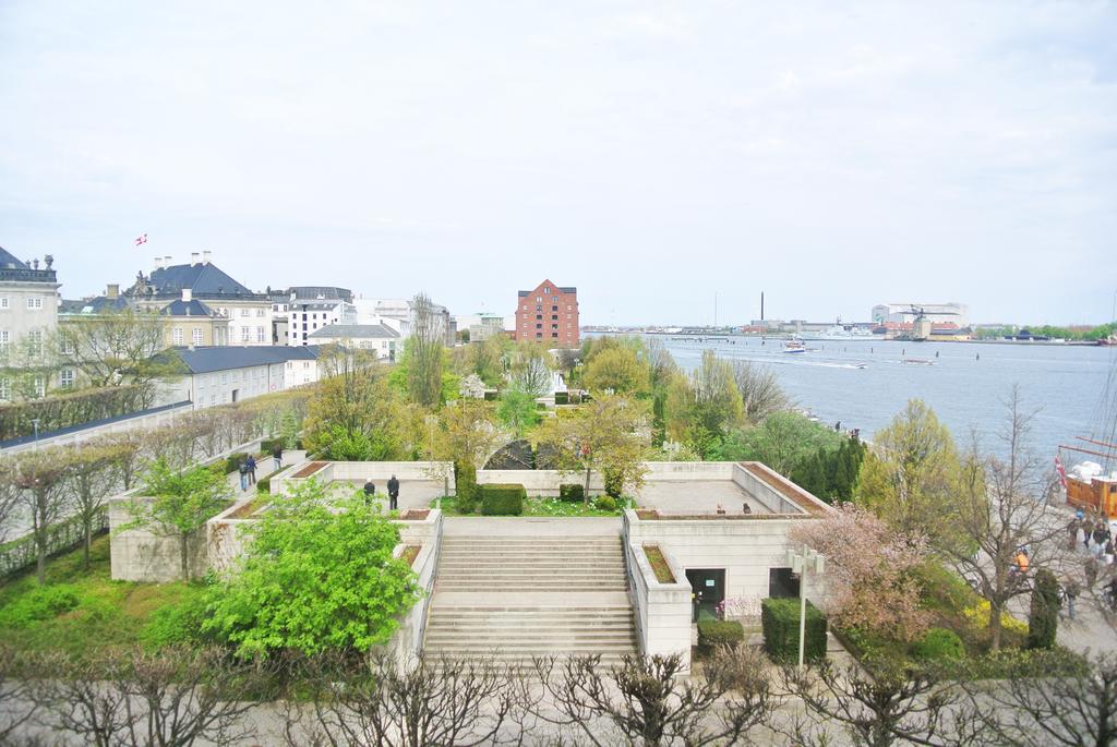 Copenhagen Admiral Hotel Esterno foto The photo shows a scenic view of a waterfront area. In the foreground, there are landscaped gardens with neatly arranged greenery, including trees and shrubs. Stone steps lead down to the gardens, inviting exploration. In the background, a river is v