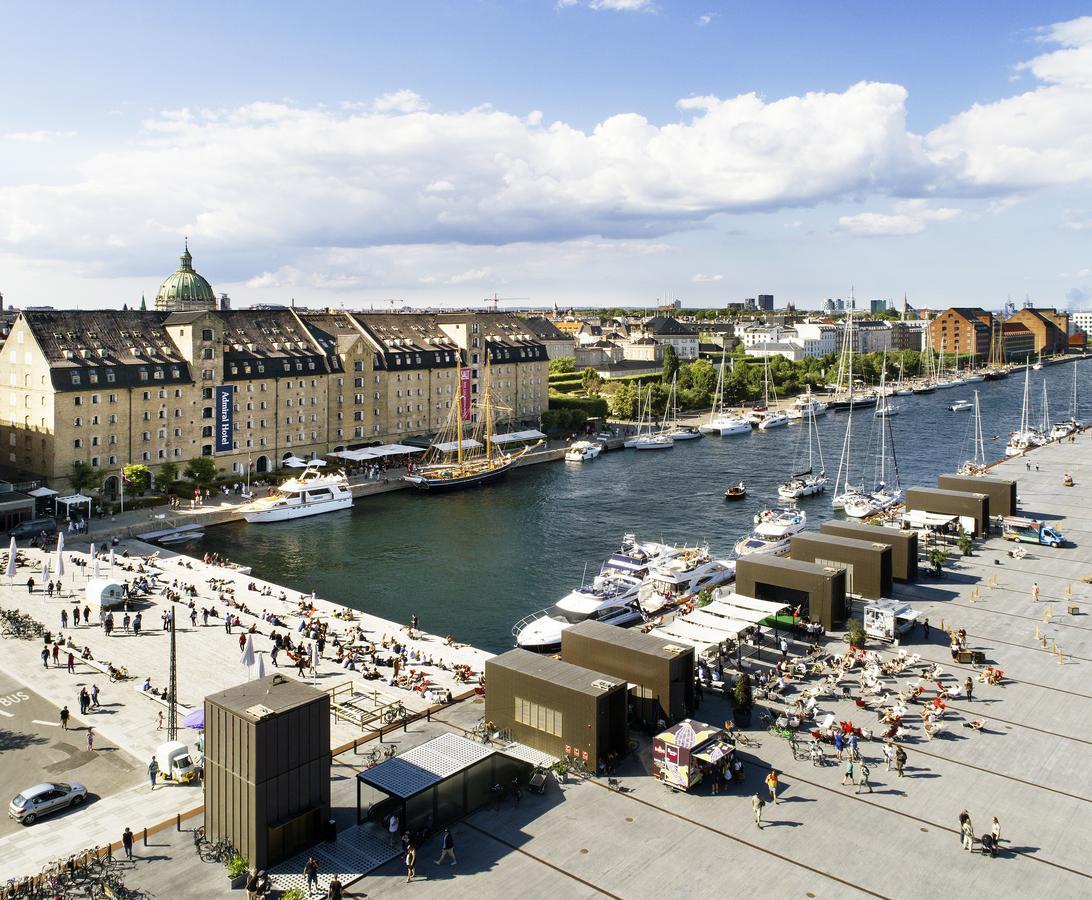 Copenhagen Admiral Hotel Esterno foto The photo shows a vibrant waterfront scene. On one side, there are several buildings with a mix of architectural styles, likely housing shops or restaurants. A canal or small river runs through the area, lined with boats and yachts. People are seen e
