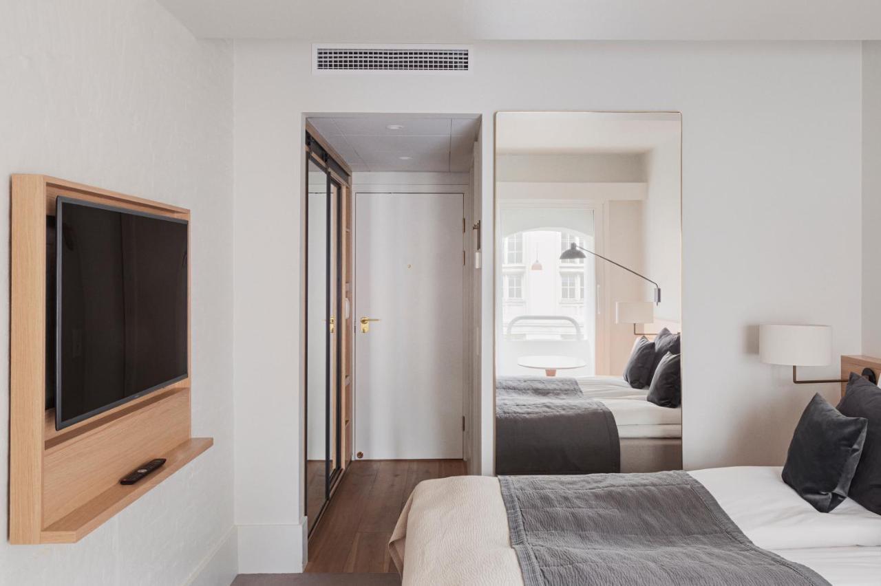 Copenhagen Admiral Hotel Esterno foto The photo shows a modern hotel room. On one side, there is a flat-screen TV mounted on the wall, along with a wooden shelf below it. There is a large mirror next to a doorway, which leads into what appears to be the entrance of the room. On the oppos